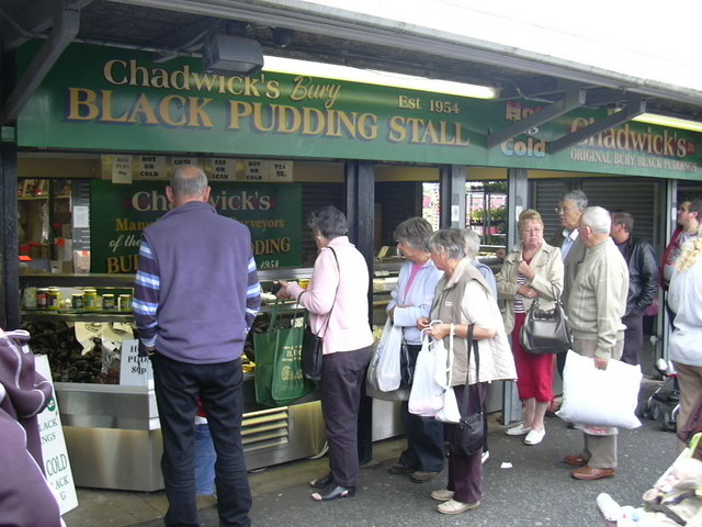 Bury: The Market, the Black Pudding & the East Lancashire Railway 3 Shoppers queuing at Chadwick's black pudding stall under its green sign at Bury Market
