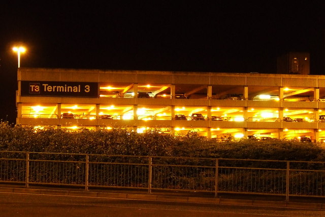The Terminal 3 multi-storey car park at Manchester Airport lit up at night, with parked cars visible across four decks and a T3 Terminal 3 sign on the facade