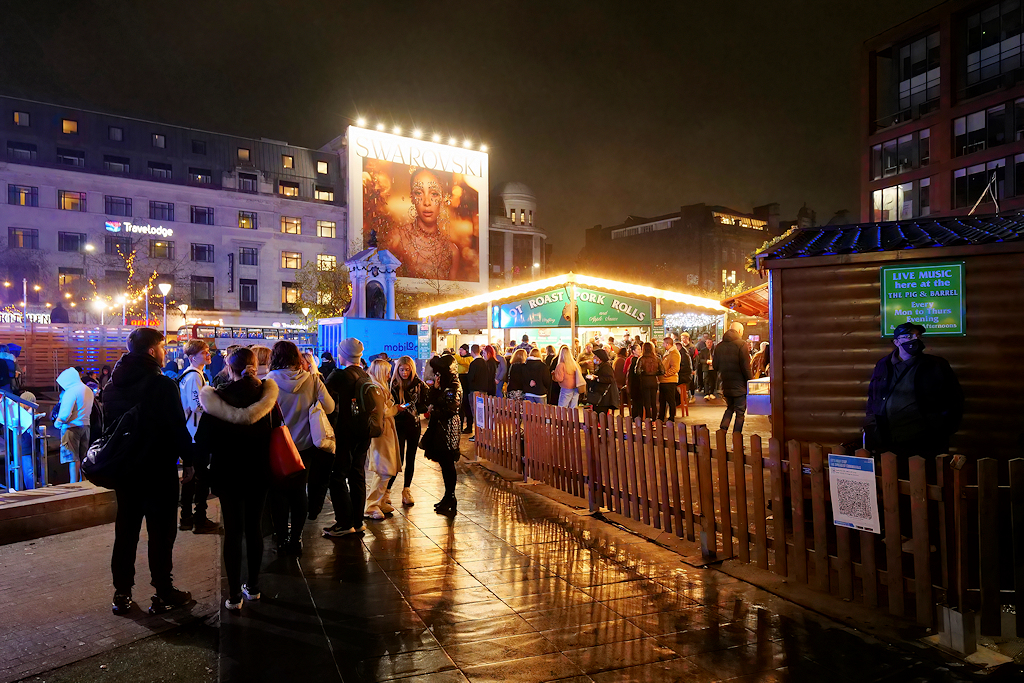 Manchester Christmas Markets Food & Drink: What to Eat & Drink 6 Crowds at the Piccadilly Gardens Christmas market at night on wet paving