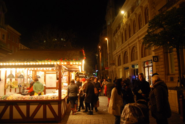Manchester Christmas Markets Tips: Best Time, Parking & Avoiding Crowds 3 Crowds browsing a lit Christmas market stall in St Ann's Square at night