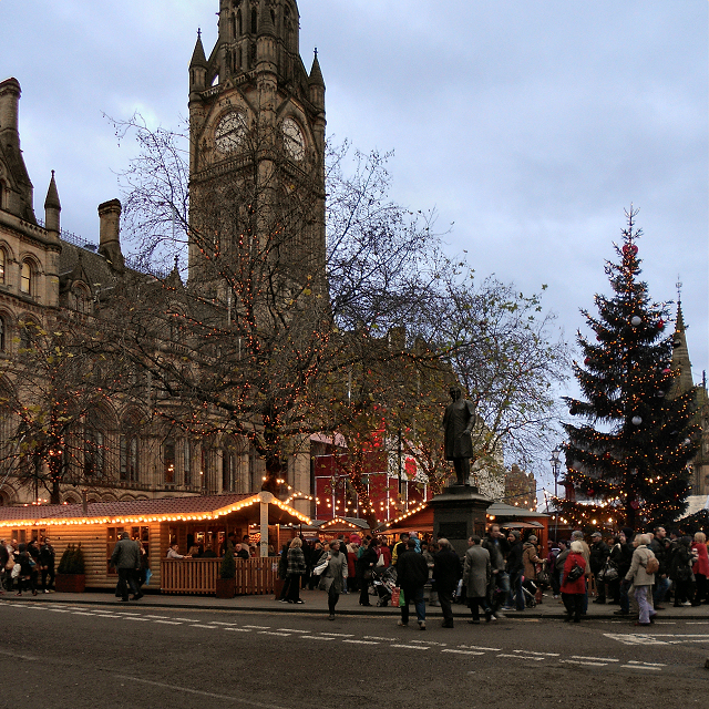 Manchester Town Hall clock tower and a large Christmas tree above crowds at the Albert Square market