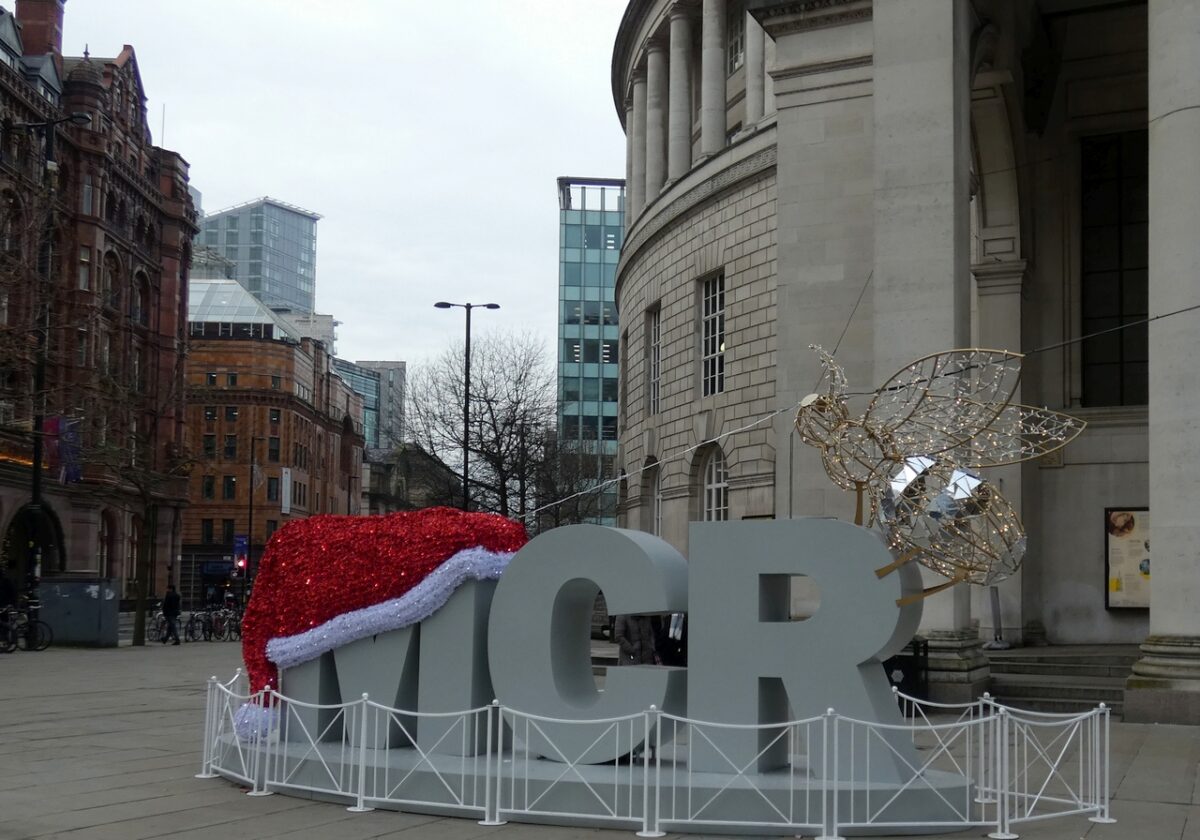 Large MCR letters wearing a red Santa hat, with a golden bee sculpture, outside Manchester Central Library