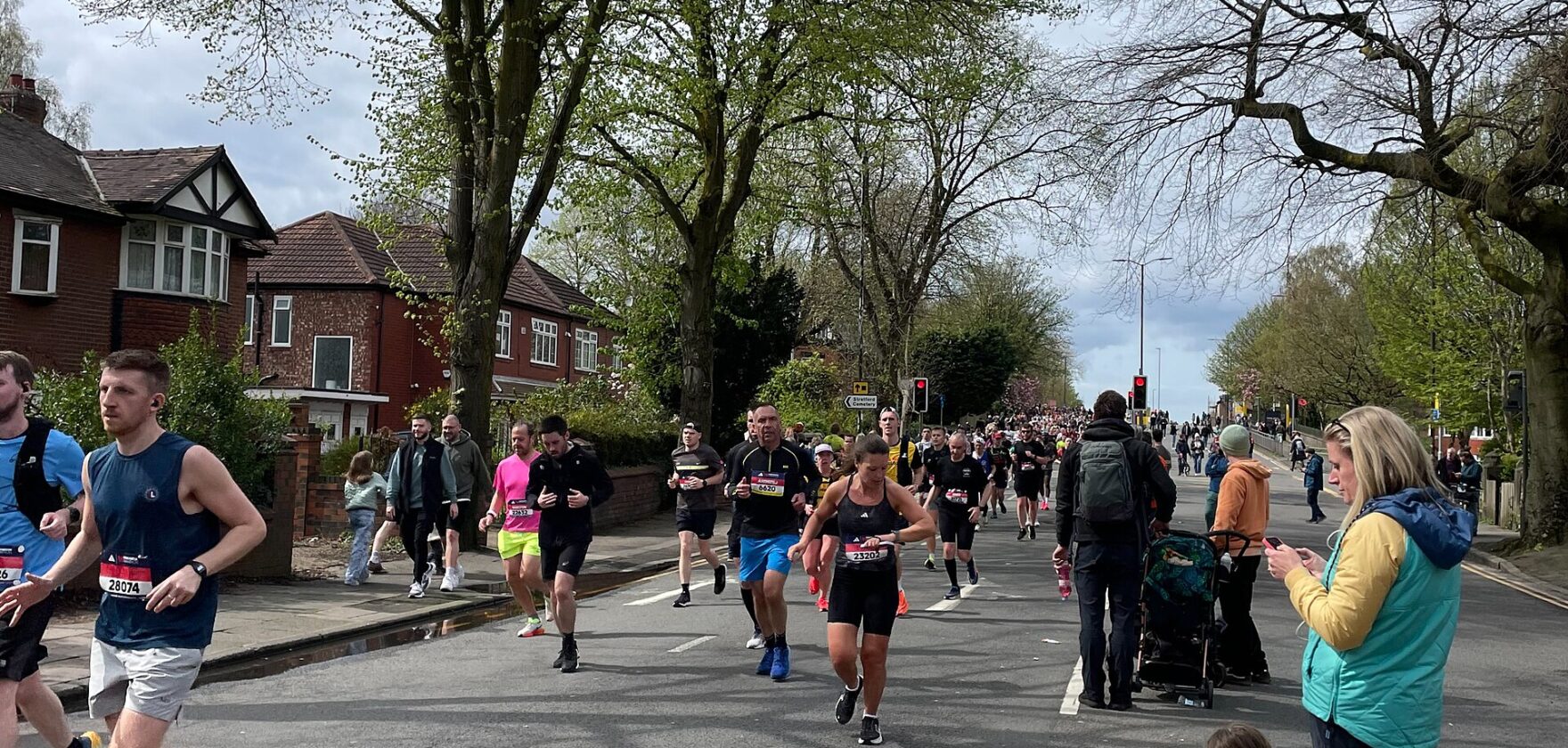 Marathon runners on a tree-lined stretch of Edge Lane in Stretford with spectators on the verge