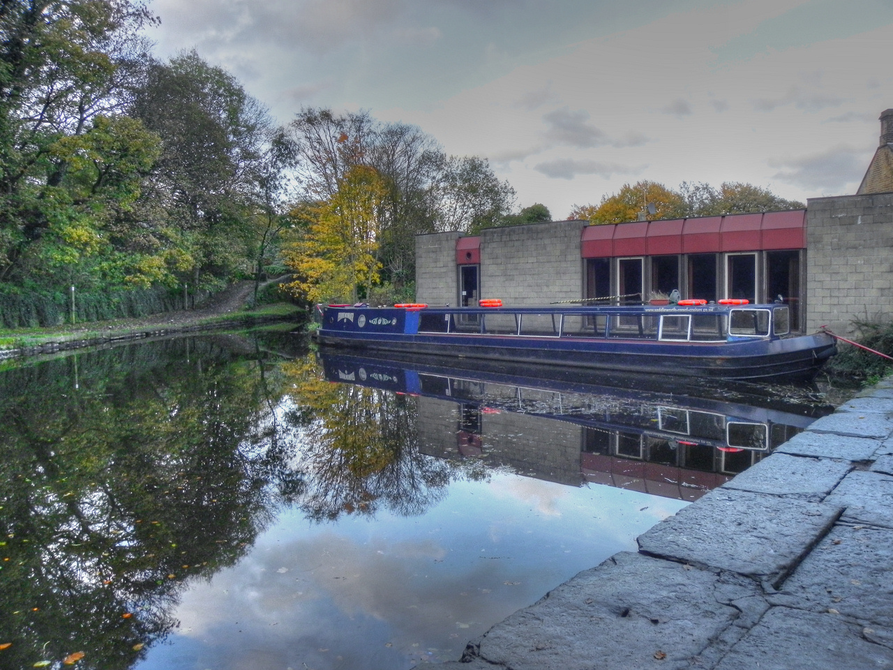 A narrowboat moored on the Huddersfield Narrow Canal at Uppermill beside a stone wharf