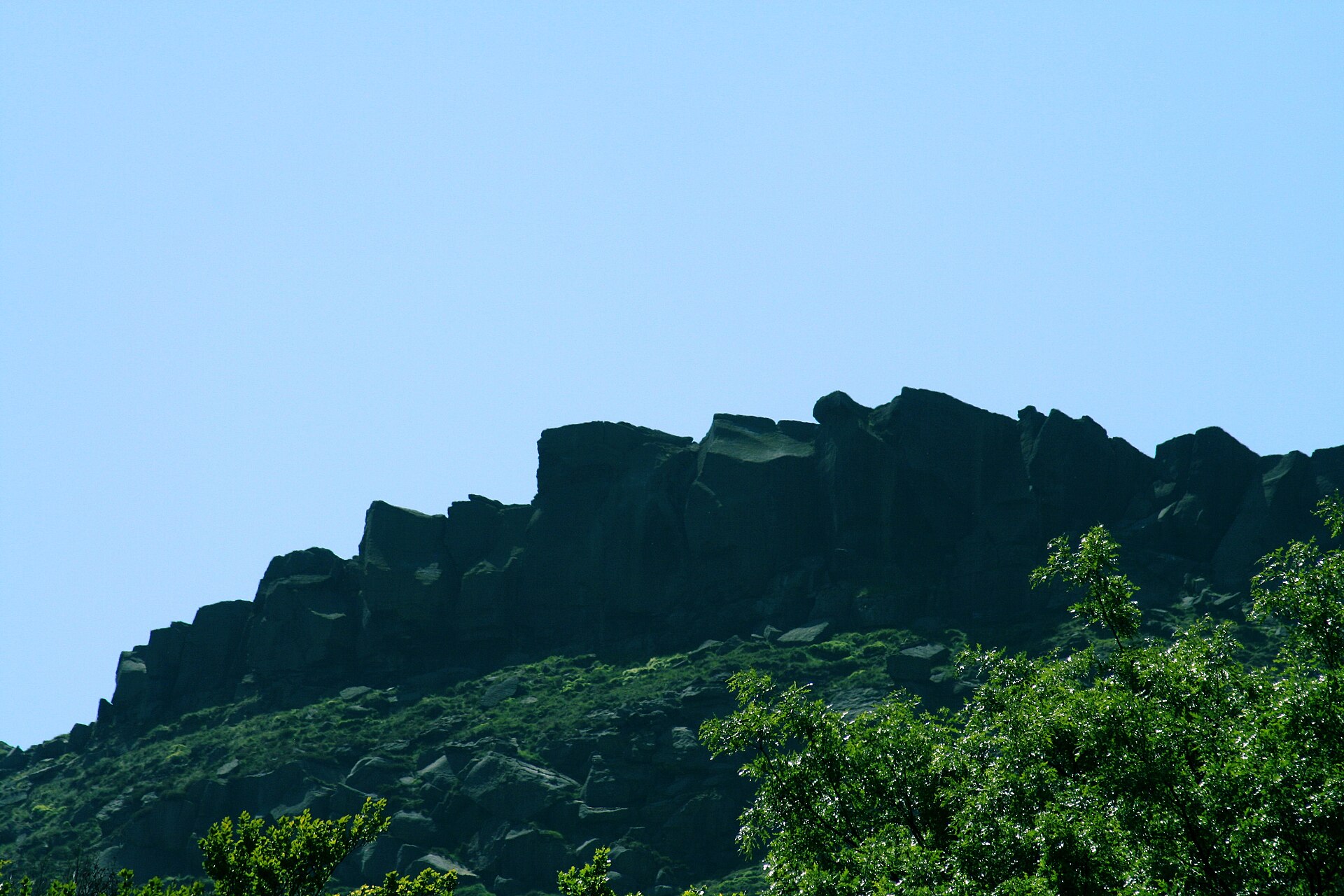 Dark gritstone rocks along a moorland edge above Dovestone Reservoir against a clear sky