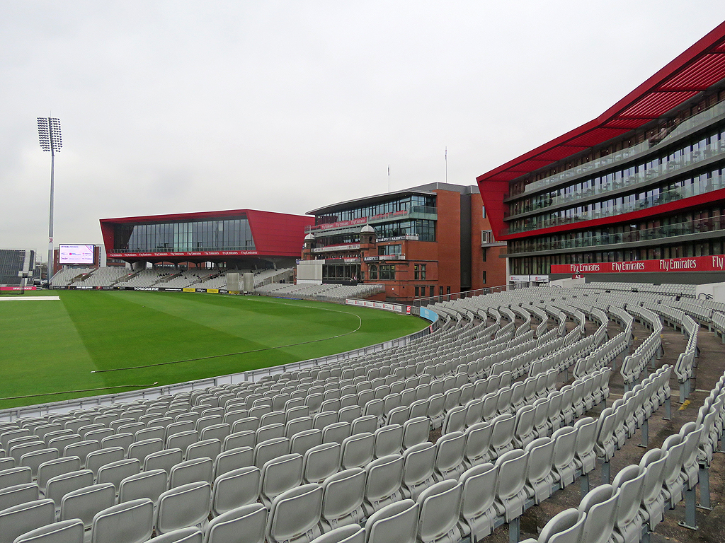 Emirates Old Trafford: Cricket, Concerts & Match Days 7 The red-framed Hilton Garden Inn building rising above empty grey seats and the outfield at Emirates Old Trafford