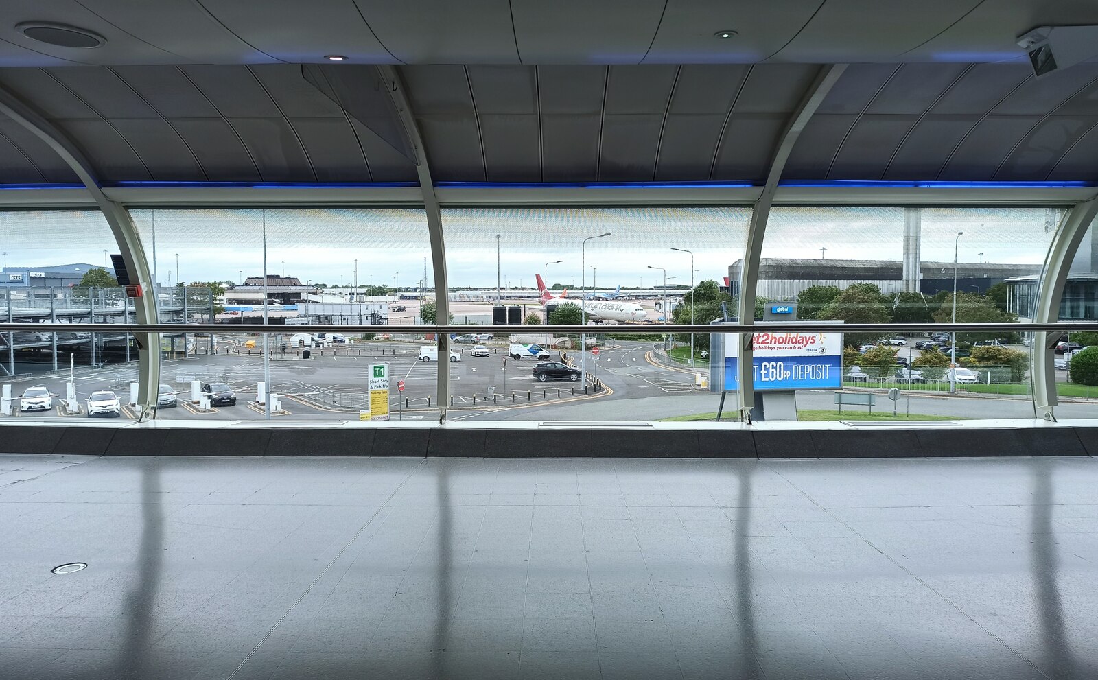 Manchester Airport Arrivals: What to Do the Moment You Land 4 Inside a glazed covered walkway at Manchester Airport looking out over a car park