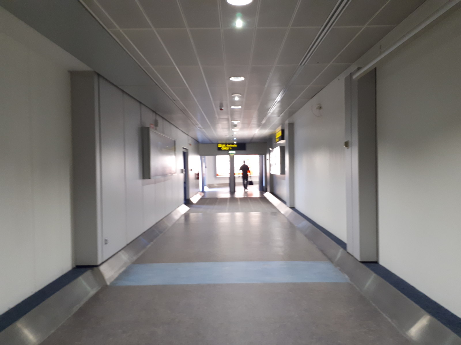 Manchester Airport Arrivals: What to Do the Moment You Land 3 A long, bright white arrivals corridor at Terminal 3, Manchester Airport, with a passenger walking at the far end