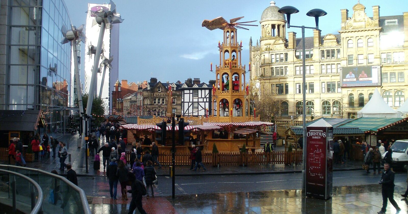 Christmas market stalls and a tall wooden Christmas pyramid in Exchange Square, Manchester, with the Corn Exchange behind