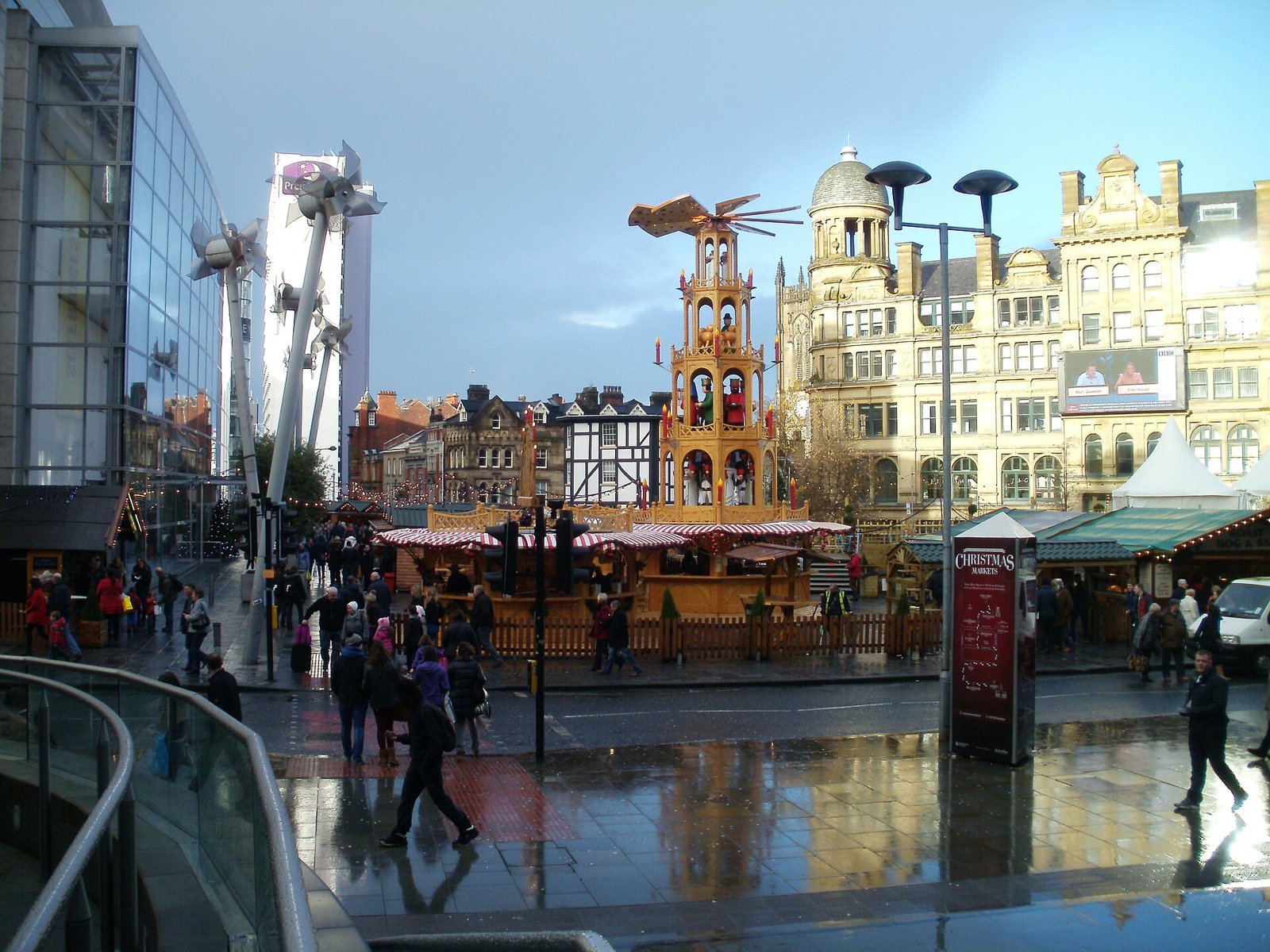 Christmas market stalls and a tall wooden Christmas pyramid in Exchange Square, Manchester, with the Corn Exchange behind