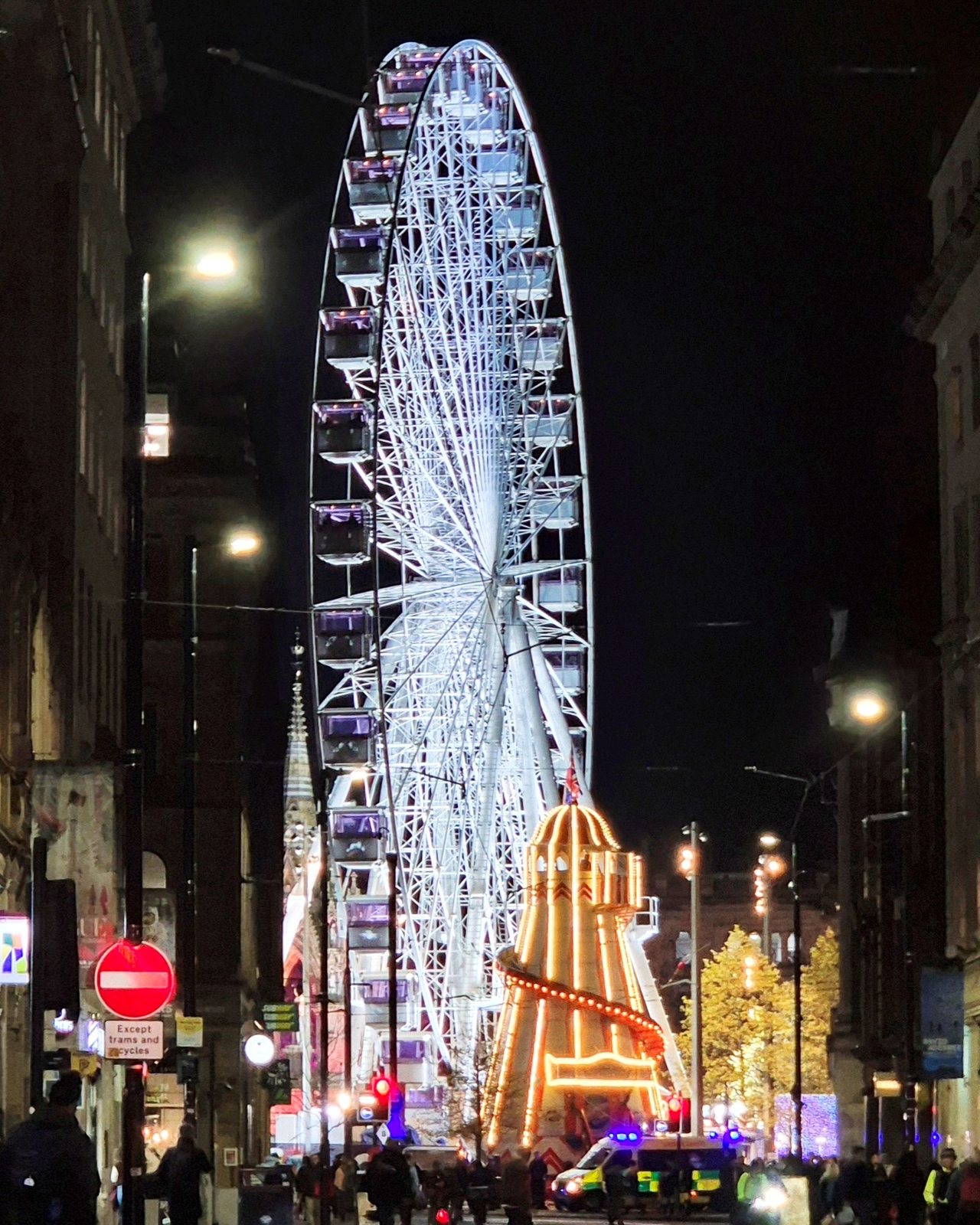 Manchester in November: Weather, Events & What to Do 4 A lit Ferris wheel and helter-skelter at the end of a city street with tram tracks, in Albert Square