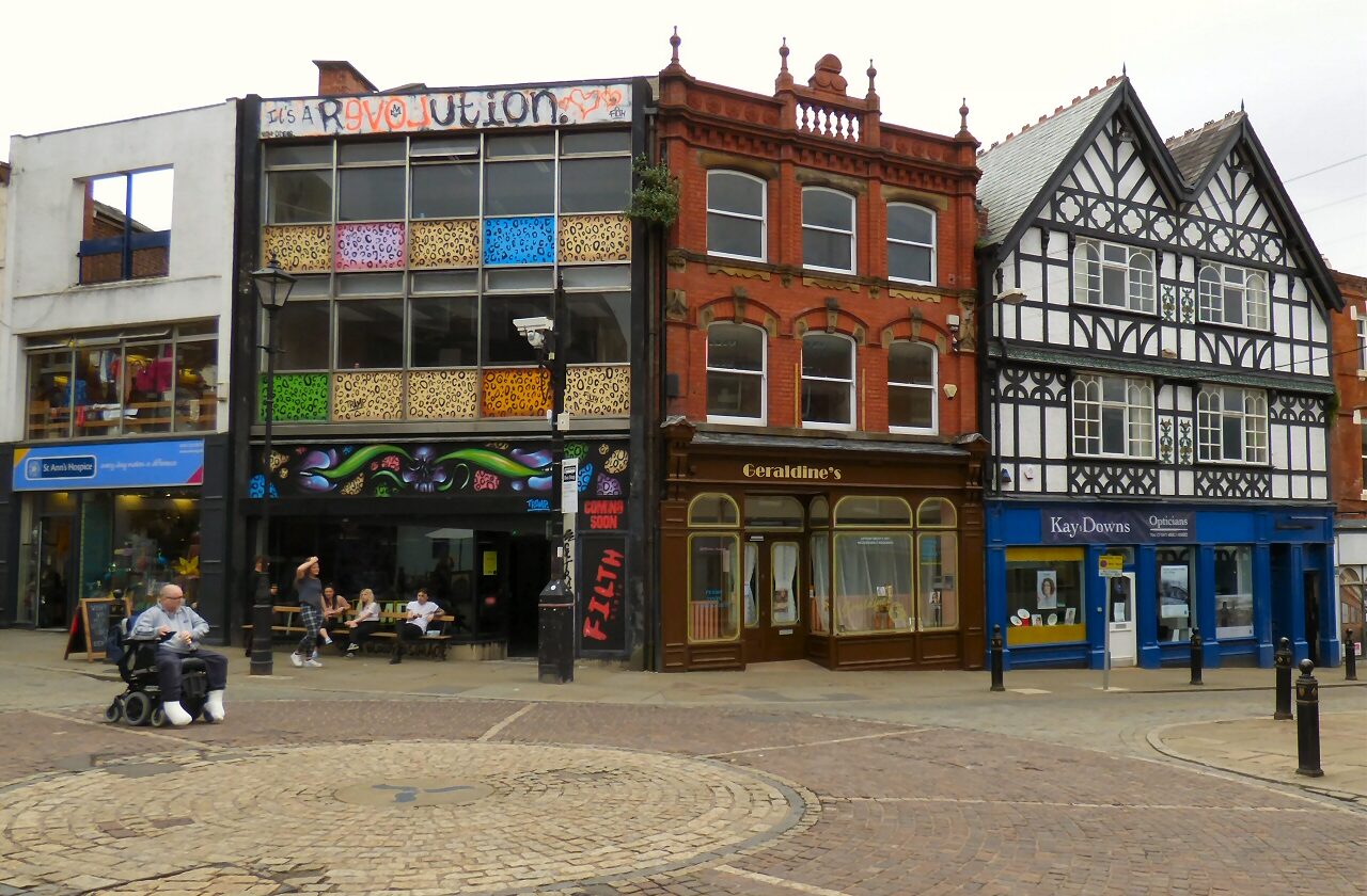 Old shopfronts, including a black-and-white timbered building, on a cobbled corner where Little Underbank meets Great Underbank in Stockport